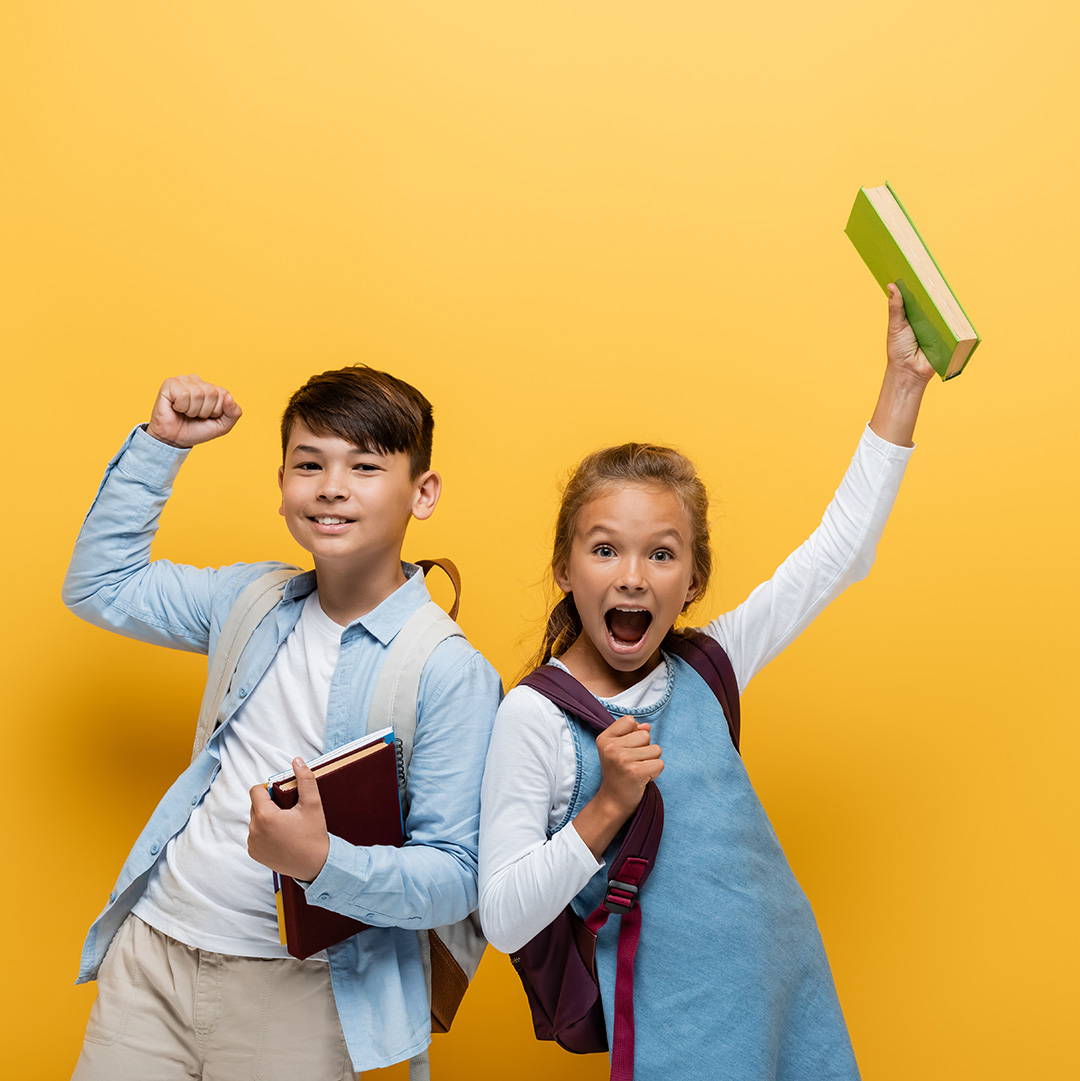 A young boy and young girl cheering with books in their hands.