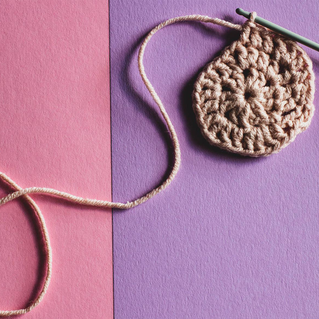 a crochet hook with brown yard on top of a pink and purple background