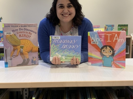 Katie Underwood leaning against a shelf of children's books holding a copy of Runaway Bunny