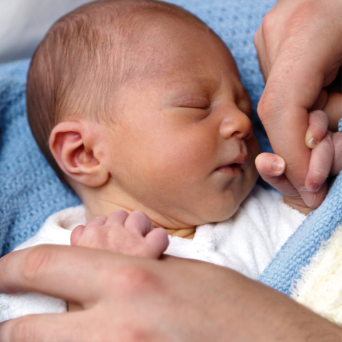 a newborn clutching the finger of an adult