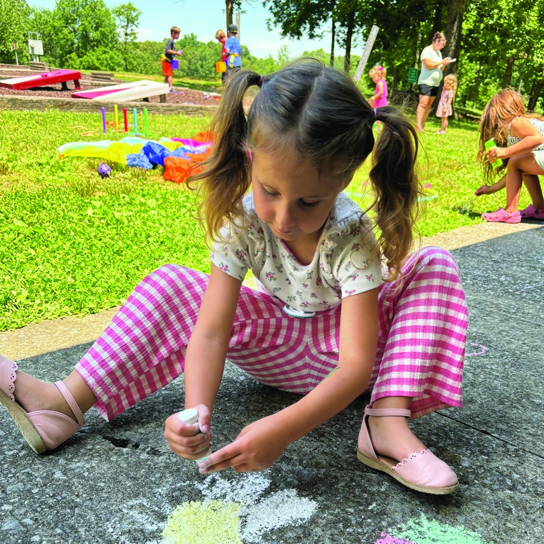 photo of a young girl in pig tails drawing on a sidewalk with chalk in a park