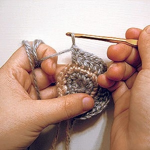 Someone crocheting a circle using grey and brown yarn